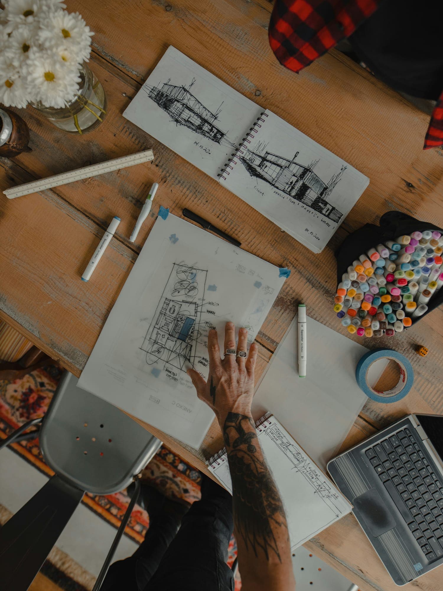 Architectural sketches, markers and a laptop on a wooden table, seen from above